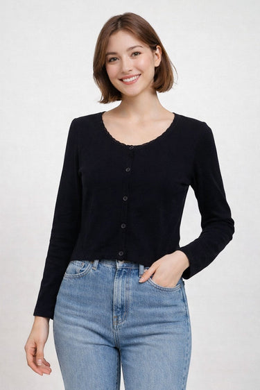 SaltTree model wearing a black ribbed knit cropped cardigan with long sleeves and a scalloped edge over blue jeans.
