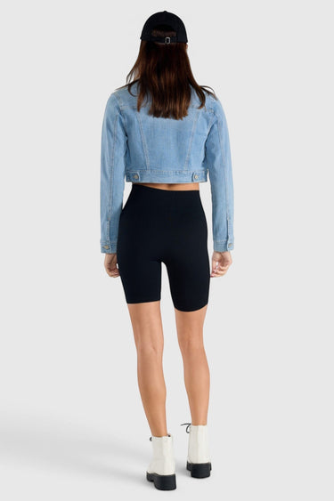 SaltTree model wearing an Enjean stone wash cropped denim jacket with black biker shorts and white boots, back view.