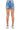 Back view of SaltTree American Bazi medium blue wash denim shorts with rhinestone trim on a model wearing sneakers.