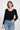 SaltTree model wearing a black ribbed knit cropped cardigan with long sleeves and a scalloped edge over blue jeans.