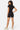 Model wearing SaltTree Love Poem black fitted zip-up polo romper with short legs, back view against white background.
